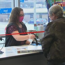 Une caissière, derrière une vitre de plexiglas, sert un client avec un masque.