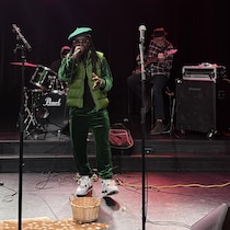Un chanteur accompagné d'un bassiste, d'un guitariste et d'un batteur sur une scène.