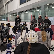 Des joueuses de hockey écoutent des instructeurs sur une patinoire.