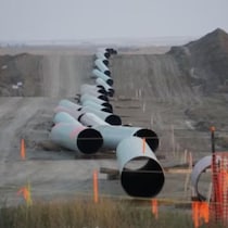 Une longue rangée de sections de pipelines de grand diamètre sont déposées bout à bout sur un terrain de construction sablonneux.