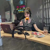Une femme assise en studio radio devant un micro, souriante, un livre posé sur la table.