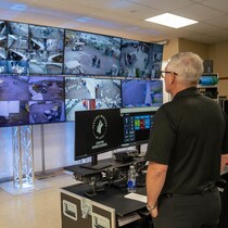 Un homme regarde des écrans sur lesquels des caméras de surveillance projettent des images.