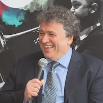Alain Trudel sourit, il tient un micro dans sa main. 