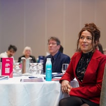 Une femme assise à une table suit une conférence.