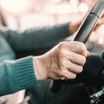 Photo rapproché d'une main d'une personne âgée sur un volant de voiture.