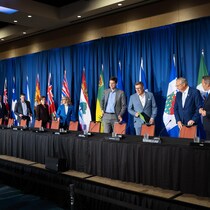Les 13 premiers ministres des provinces et des territoires du Canada s'apprêtant à s'asseoir à une longue table pour une conférence de presse. 