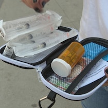 Une main humaine ouvre une trousse de naloxene et montre son contenu dont plusieurs seringues neuves