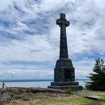 Une croix de pierre érigée devant le fleuve Saint-Laurent.