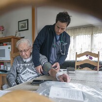 L'infirmier prend la pression d'un patient dans la salle à manger de ce dernier.