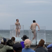 Sur une plage un public observe deux personnes danser dans des cubes remplis d'eau.