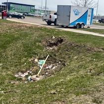 Des déchets variés sont sur l'herbe, près d'un supermarché. 