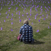 Une femme est agenouillée de dos, devant des petits drapeaux mauves