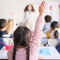 Des écoliers lèvent la main dans une salle de classe.
