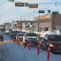 Des voitures circulent sur une chaussée partiellement enneigée et bordée de bancs de neige dans une zone de travaux urbains.