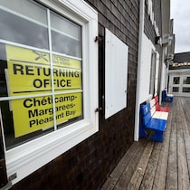 Une affiche jaune dans une fenêtre et un banc peint aux couleurs du drapeau acadien.
