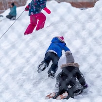 Des enfants de niveau primaire qui jouent sur une butte de neige dans un cour d'école.
