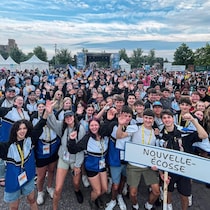 Des centaines de jeunes lèvent les bras devant une scène de spectacle en plein air.