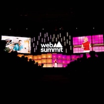 Une conférencière vêtue de rouge parle sur une scène. On peut lire les mots Web Summit plus haut.