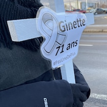 Une femme tient une croix blanche avec le nom d'une femme victime d'un féminicide.