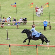 Une femme brandit une épée sur le dos d'un cheval en plein galop.