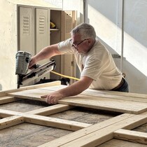 Un homme perce des planches de bois dans un atelier. 