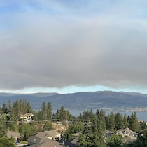 Photo en plongée montrant une nappe de fumée gris-brun dans le ciel au-dessus d'une ville (West Kelowna) et d'un grand lac (lac Okanagan).
