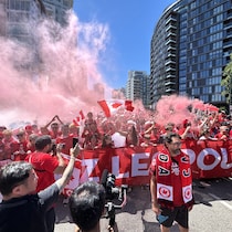 Des supporteurs en rouge avec une banderole et des fumigènes, dans les rues de Vancouver.