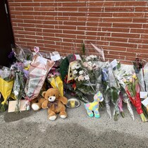 Plusieurs bouquets de fleurs, trois peluches et une chandelles sont déposées près d'un des murs de brique de l'école. Des messages de condoléances sont inscrits sur les cartes accompagnant les bouquets de fleurs. 