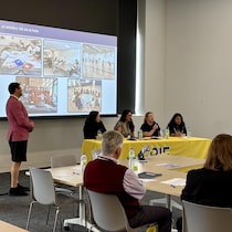 Des personnes assises écoutent un panel auquel participent quatre femmes. Un écran est sur le mur.