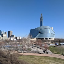 Le Musée canadien des droits de la personne vu de l'extérieur en plan large, entouré d'espaces verts, avec des bâtiments du centre-ville de Winnipeg en arrière-plan. 