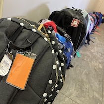 Des sacs d'école remplis de matériel sont alignés le long d'un couloir.