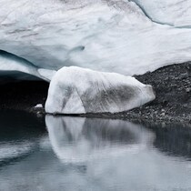 Un glacier sur le bord de l'eau laisse entrevoir des zones de pierre en raison de sa fonte.