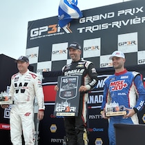 Trois hommes en tenue de pilote de course sur un podium