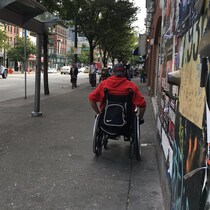 Un homme en fauteuil roulant se déplace sur le trottoir près d'un arrêt d'autobus abandonné.