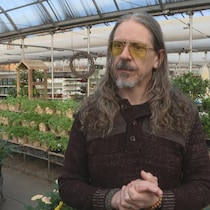 Un homme se tient debout dans une serre remplie de plantes vertes.