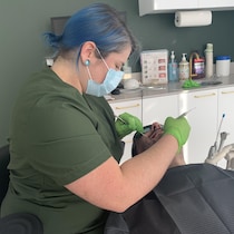 Cassandra Gilbert, masque au visage, examine un patient à l'aide de deux instruments.
