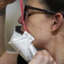 Profil gauche d'une femme portant des lunettes. Elle retire un masque médical de protection et on voit sur sa joue les traces laissées par les élastiques du masque.