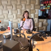 Une femme souriante est assise à une table ronde dans un studio de radio, devant un microphone.