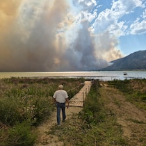 Un homme regarde la fumée qui s’élève d’un feu de forêt sur l’autre rive d’un lac.