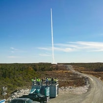 Une fusée s'élève dans un ciel bleu au-dessus d'une forêt de conifères, une fine traînée de fumée blanche s'échappant de sa trajectoire.