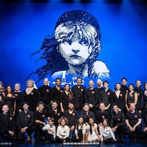 Les comédiens et comédiennes posent sur scène devant l'affiche de la comédie musicale. 