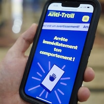 Une main qui tient un téléphone avec un avertissement contre un intimidateur.