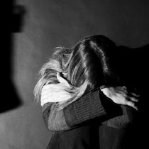Une femme assise, se cachant les yeux pour ne pas voir son partenaire violent.