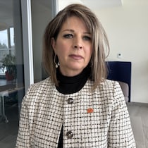 Une femme debout dans un bureau terne, près d'une baie vitrée.