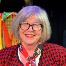 Madeleine Blais-Dahlem, une femme souriante aux cheveux courts gris-blanc. Elle porte des lunettes à monture noire. Elle est vêtue d'un blazer à motifs rouge et noir.