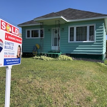 Une maison modeste avec une affiche d'une agente immobilière sur la pelouse avant.