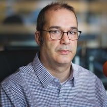 Un homme portant des lunettes assis dans un studio. 