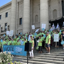 Des manifestants vêtus de chandail vert brandissent des affiches et sont sur les marches du Palais législatif de Winnipeg, le 24 avril 2023. 