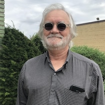 Photo d'un homme souriant aux cheveux et barbe blancs qui porte des lunettes fumées