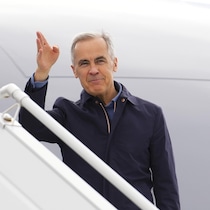 Mark Carney monte à bord d'un avion. 
